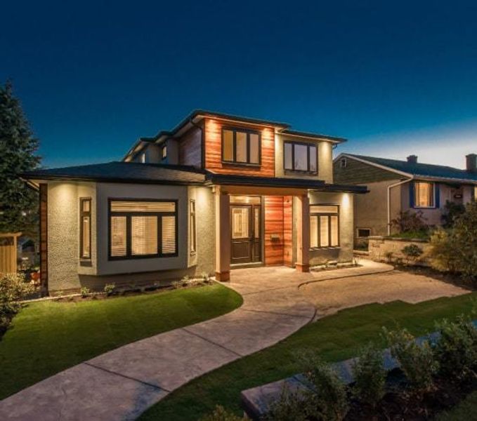 Big, luxury modern house at dusk with the lights on and windows lit up